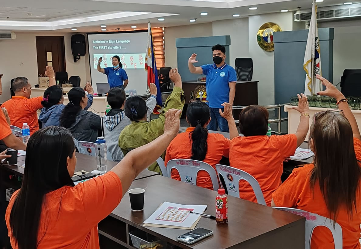 MCCID Deaf Tutors' Alexandra Dominguez and Elizar Bic Pongos teach fingerspelling to employees of Caloocan City Hall.